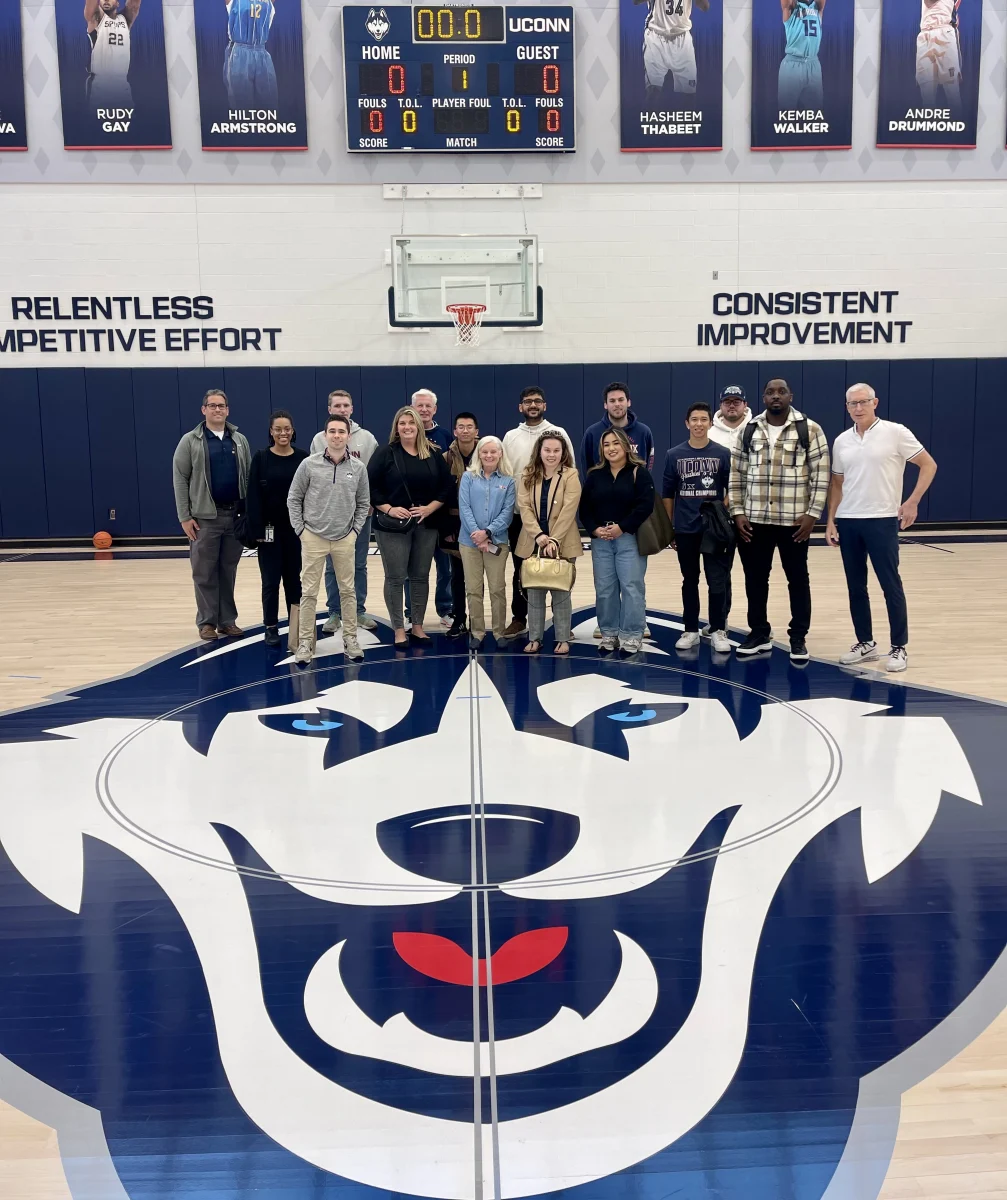 Student group standing on the floor of Gampel Pavillion with the UConn Husky logo.